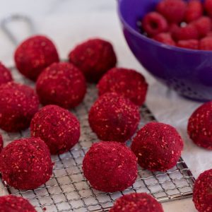 raspberry bliss balls on top of a wire rack next to a bowl of raspberries