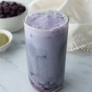 iced blueberry matcha latte with a white napkin in the background along with a bowl of matcha and a bowl of blueberries