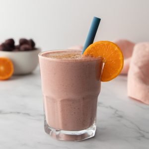 a chocolate cherry smoothie in a glass cup with an orange slice on the rim and a bowl of cherries in the back