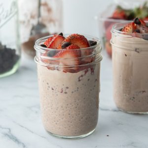 chocolate chia pudding in glass jars with strawberries on top and a jar of chocolate chips in the background